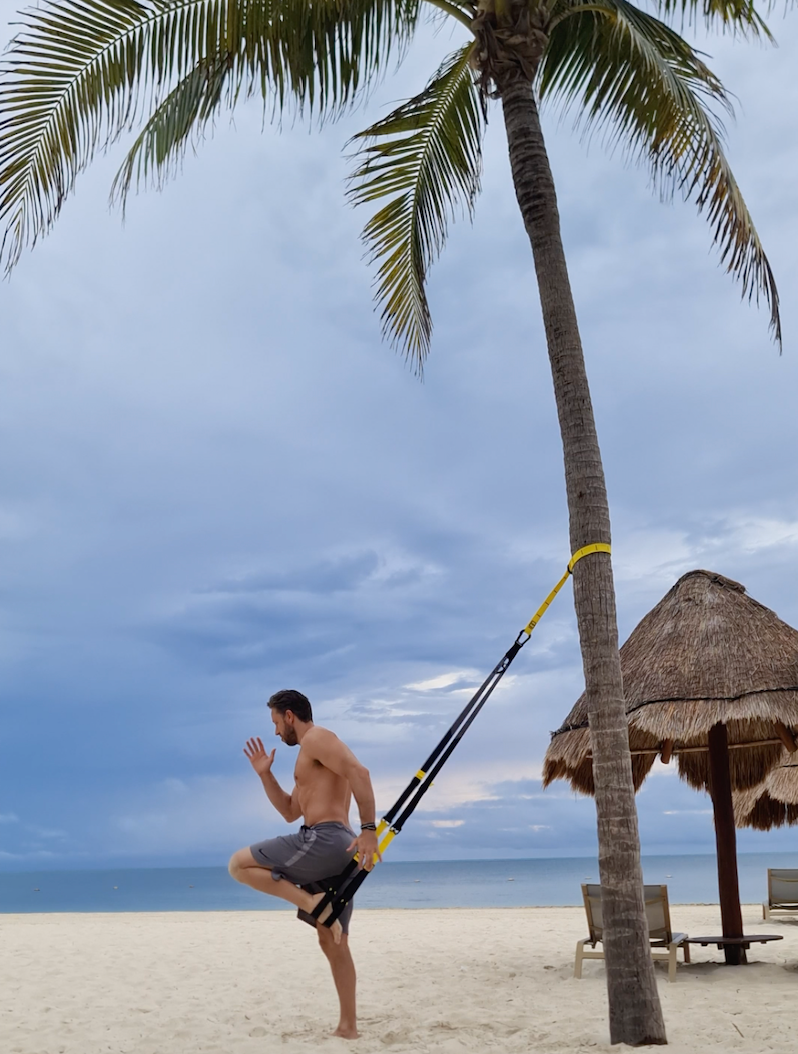 Louis Lopez holds his TRX Suspension Trainer in front of a black, yellow, and white background
